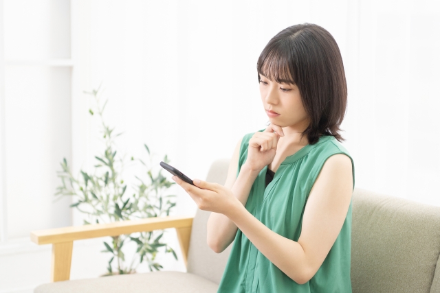 スマートフォンを持ちながら困っている女性のイメージ。